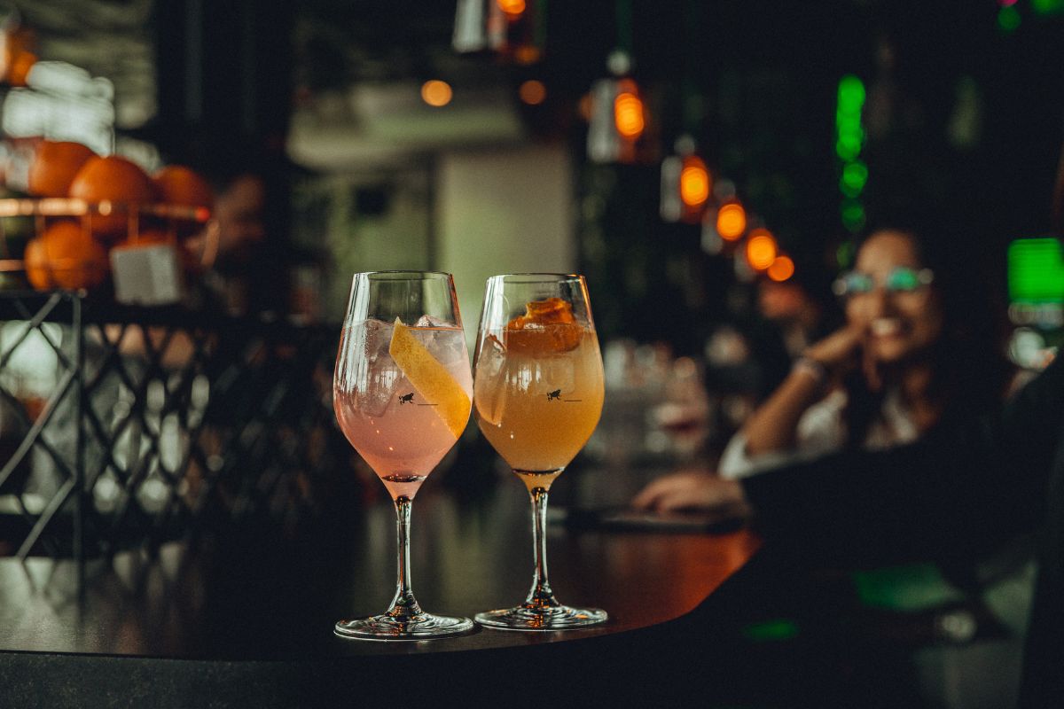 Two glasses of wine with orange slices on the rim, placed on a polished bar surface.